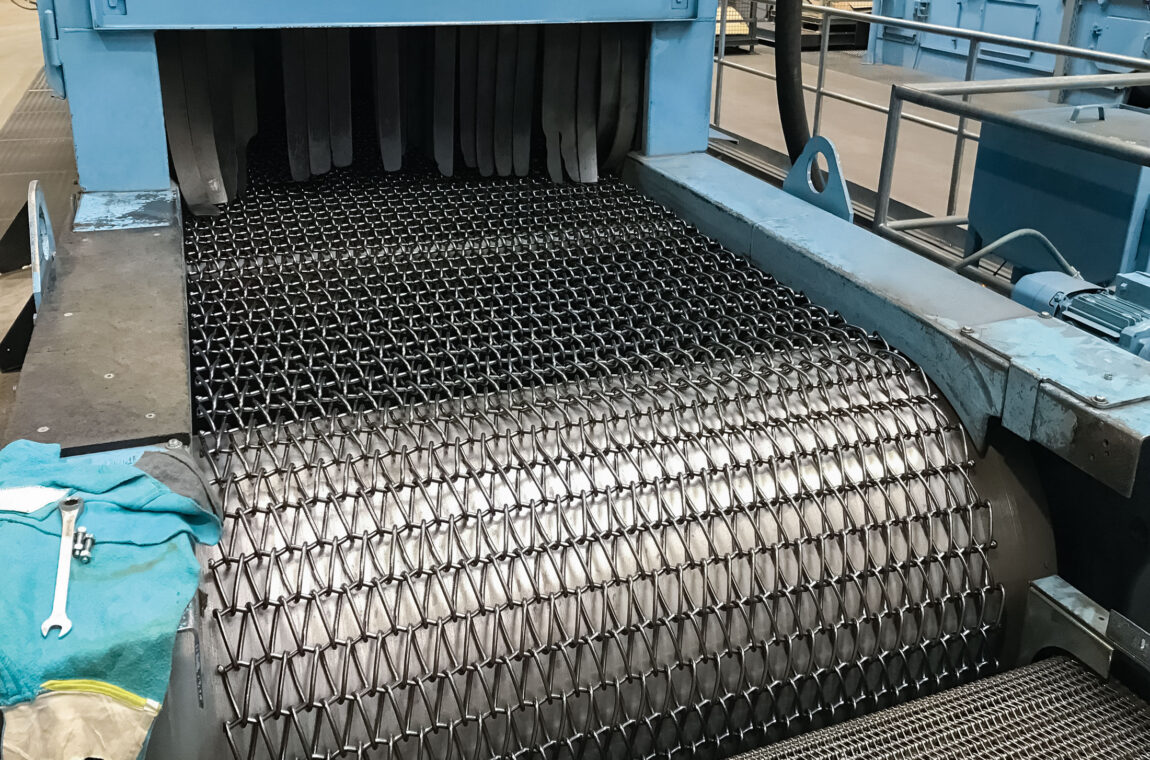 Installation und Montage eines neuen STEINHAUS Ersatzgurtes auf der Umlenktrommel einer industriellen Sandstrahlanlage während einer Wartung.